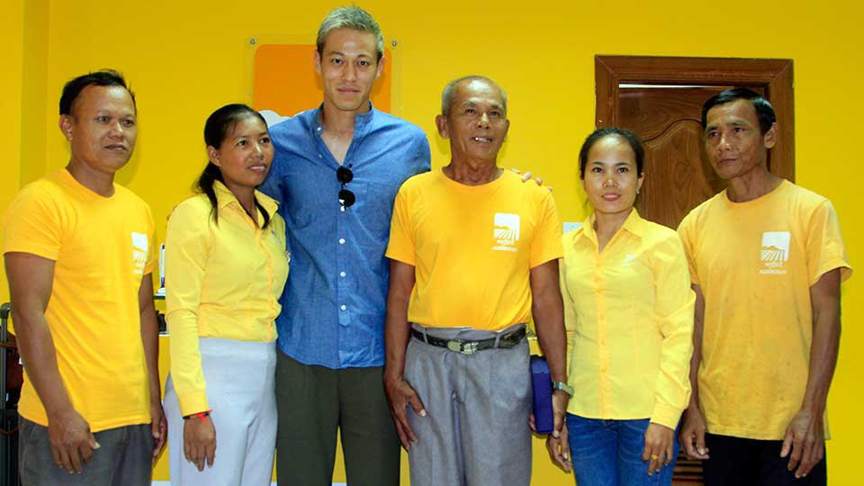 លោក កេស៊ូកិ ហុងដា (Keisuke Honda) កីឡាករ​បាល់ទាត់​ជប៉ុន និង​​ជា​គ្រូ​បង្វឹក​កីឡាករ​​បាល់​ទាត់​ជម្រើសជាតិ​កម្ពុជា ថតរូប​ជាមួយ​កសិករ​និងបុគ្គលិក​ក្រុមហ៊ុន អេហ្គ្រីបាឌី (Agribuddy)។