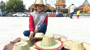 កញ្ញា សុខ ស្រីល័ក្ខ អាយុ ២៩ឆ្នាំ អង្គុយ​លក់​មួក​ត្នោត​ នៅ​មាត់​ទន្លេ នៅថ្ងៃទីមួយ​នៃ​ពិធី​បុណ្យ​អុំ​ទូក។ រូបភាព៖ សូរ ចាន់ណា