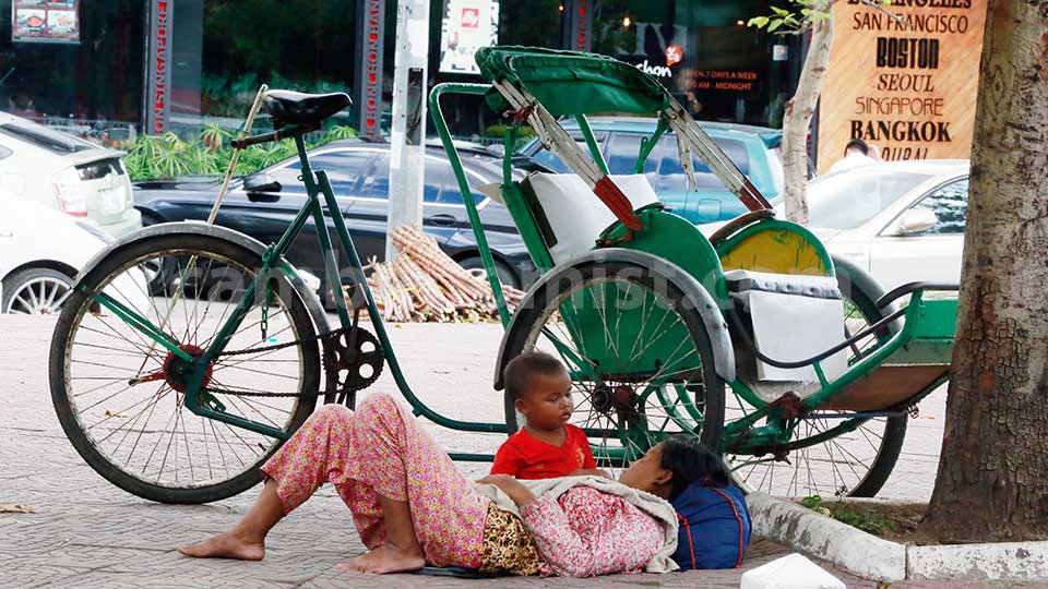 ស្ត្រី​ម្នាក់​សម្រាក​ថ្ងៃ​ត្រង់​ក្រោយ​បាយ នៅ​ក្រោម​ដើម​ឈើ​ ក្បែរ​ស៊ីក្លូ​របស់​ប្ដី នៅ​មុខ​អគារ​ ភ្នំពេញ សិនធ័រ ផ្លូវ​សុធារស រាជ​ធានី​ភ្នំពេញ។